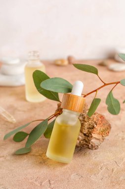 Composition with bottle of serum, stone and eucalyptus branch on color table
