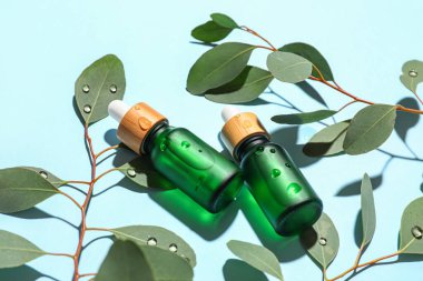 Bottles of serum and eucalyptus branches on color background