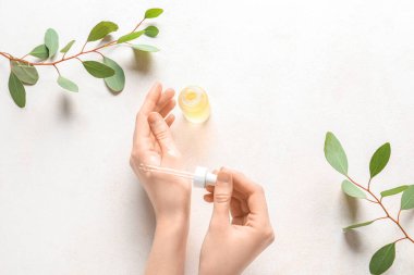 Female hands with bottle of serum and eucalyptus branches on light background