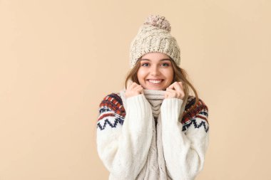 Frozen young woman in winter clothes on beige background