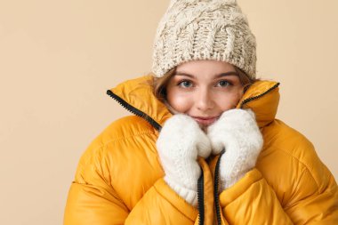 Frozen young woman in winter clothes on beige background, closeup
