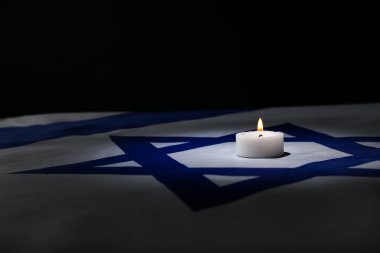 Burning candle on flag of Israel against dark background with space for text. International Holocaust Remembrance Day