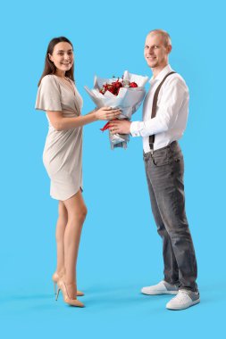 Young man greeting his wife with bouquet of flowers on blue background. Valentine's Day celebration