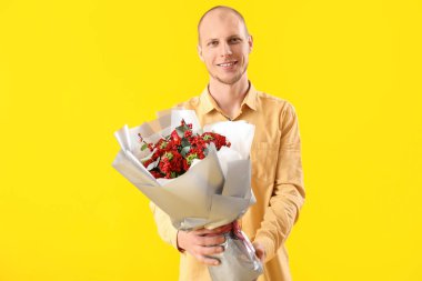 Young man with bouquet of flowers on yellow background. Valentine's Day celebration