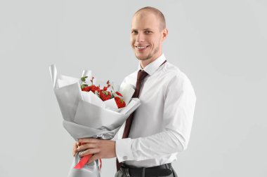 Young man with bouquet of flowers on light background. Valentine's Day celebration