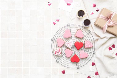 Composition with tasty heart shaped cookies, cups of coffee and gift box on light tile. Valentine's Day celebration