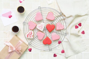 Composition with tasty heart shaped cookies, cups of coffee and gift box on light tile. Valentine's Day celebration