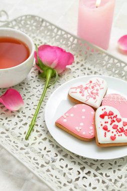 Tray with plate of tasty heart shaped cookies, cup of tea and rose flower on table, closeup. Valentine's Day celebration