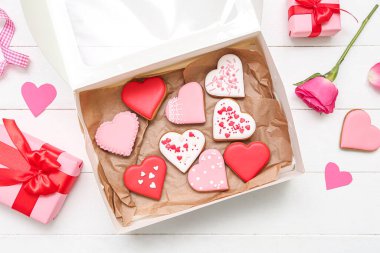 Box with tasty heart shaped cookies, gifts and rose flower on light wooden background. Valentine's Day celebration