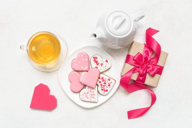 Composition with plate of tasty heart shaped cookies, gift box and cup of tea on light background. Valentine's Day celebration