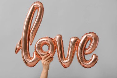 Female hand with balloon in shape of word LOVE on grey background. Valentine's Day celebration