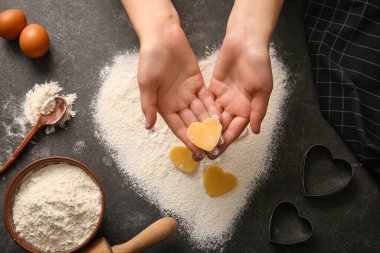 Female hands with raw cookie, flour and eggs on dark background. Valentines Day celebration