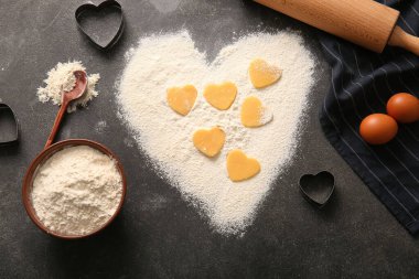 Composition with raw cookies, flour, cutters and eggs on dark background. Valentines Day celebration