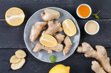 Plate with ginger roots, slices, lemon pieces and honey on dark wooden background