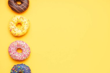 Line made of different delicious donuts on yellow background