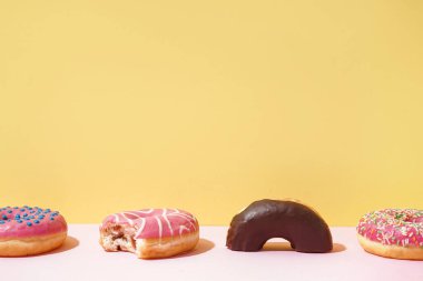 Different delicious donuts on pink table near yellow wall