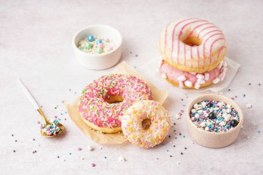 Parchments with different delicious donuts and bowls of sprinkles on white table