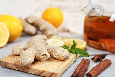Ginger root, cinnamon, lemon and teapot on wooden table, closeup