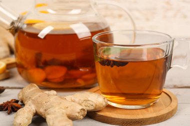 Ginger root, glass cup of black tea and teapot on wooden table