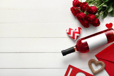 Bottle of wine, rose flowers, envelope and hearts on white wooden background. Valentine's Day celebration