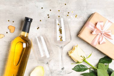 Bottle of wine, gift box, rose flower and glasses on grey table. Valentine's Day celebration