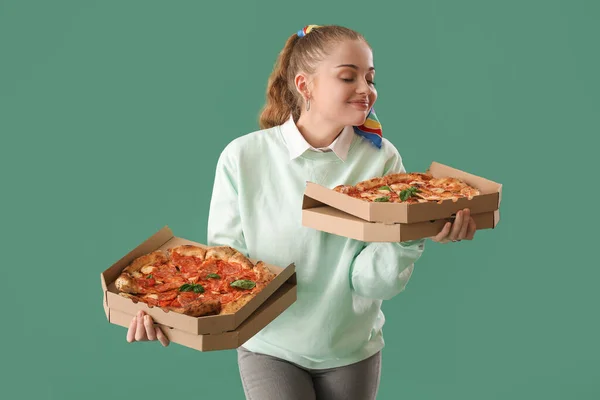 Young woman with boxes of tasty pizza on green background