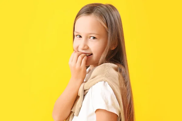 Little girl biting nails on yellow background, closeup