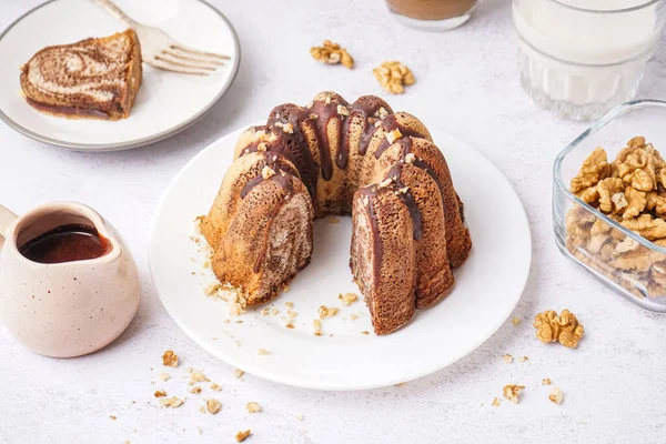 Plate with delicious cake, hot chocolate and walnuts on light background