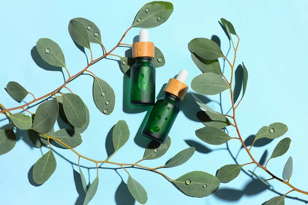 Bottles of serum and eucalyptus branches on color background