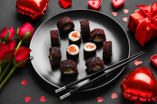 Plate with sushi rolls, chopsticks, roses and decor on black background. Valentine\'s Day celebration