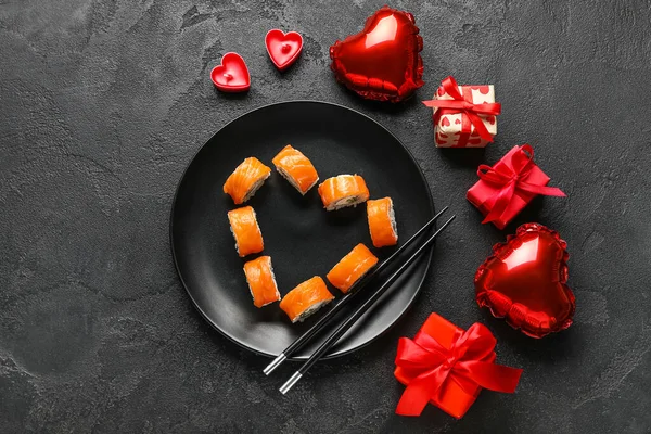 Plate with sushi rolls, chopsticks, gifts and decor on dark background. Valentine\'s Day celebration