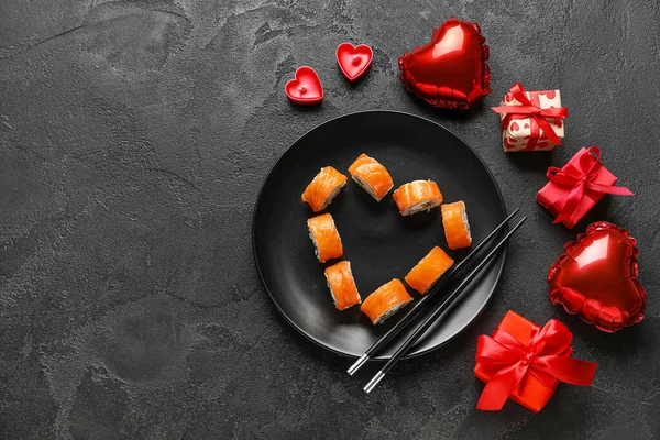 Plate with sushi rolls, chopsticks, gifts and decor on dark background. Valentine\'s Day celebration