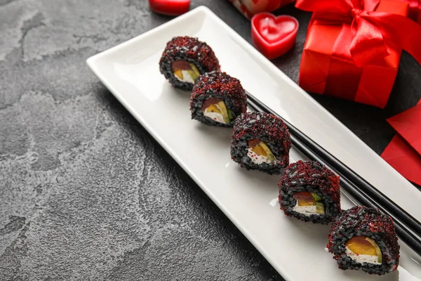 Plate with sushi rolls and chopsticks on dark background, closeup. Valentine\'s Day celebration