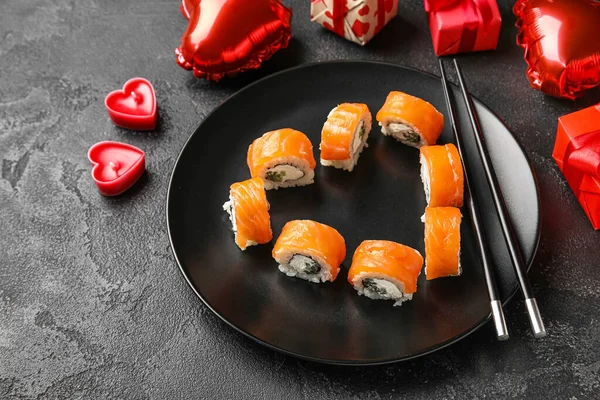 Plate with sushi rolls, chopsticks and gifts on dark background, closeup. Valentine\'s Day celebration