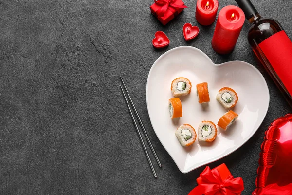Plate with sushi rolls, candles and wine bottle on dark background. Valentine\'s Day celebration