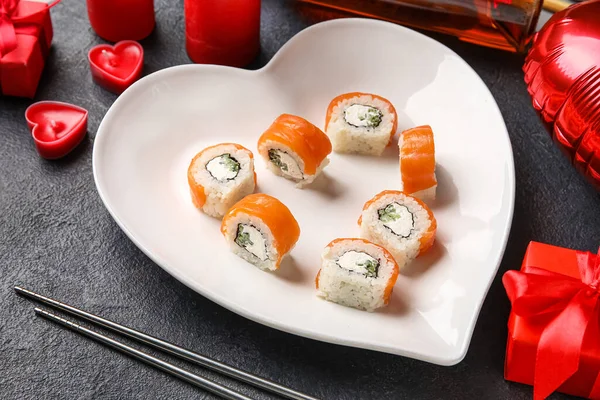 Plate with sushi rolls, chopsticks and candles on dark background, closeup. Valentine\'s Day celebration