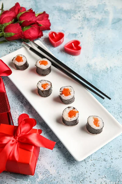 Plate with sushi rolls, chopsticks and gifts on grunge background, closeup. Valentine\'s Day celebration