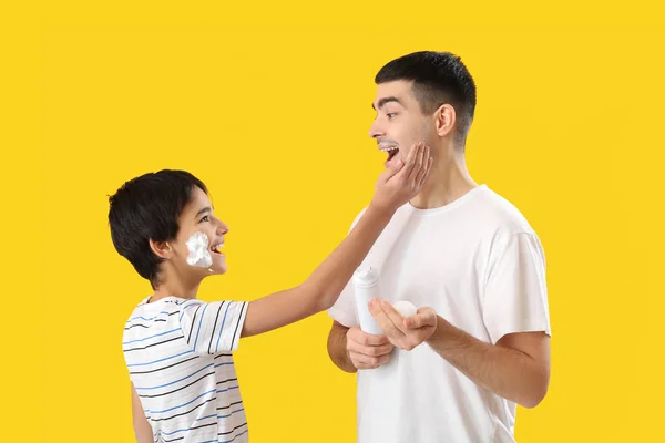 男人和他的小儿子带着黄色背景的泡沫刮胡子 — 图库照片
