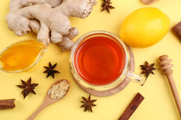 Ginger roots, cup of black tea, lemon, honey and anise on yellow background