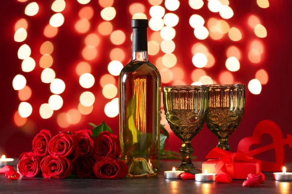 Bottle of wine, rose flowers, glasses and burning candles on black table against blurred lights. Valentine\'s Day celebration