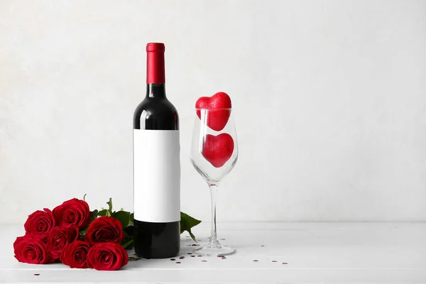 Bottle of wine, rose flowers and hearts in glass on white background. Valentine\'s Day celebration