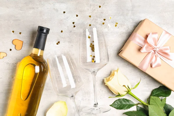 Bottle of wine, gift box, rose flower and glasses on grey table. Valentine's Day celebration