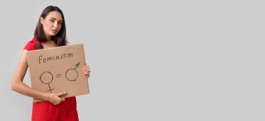 Female worker holding cardboard with symbols of man and woman on light background with space for text. Concept of feminism