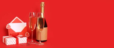 Glasses of champagne, bottle, gift and envelope on red background with space for text. Valentine's Day celebration