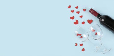 Bottle of wine, glasses and hearts on light blue background with space for text. Valentine's Day celebration