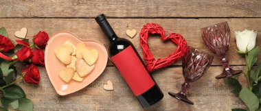 Bottle of wine, heart-shaped cookies, glasses and rose flowers on wooden background. Valentine's Day celebration