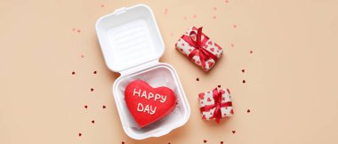 Plastic lunch box with tasty bento cake and gifts on beige background. Valentine's Day celebration