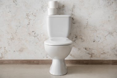 Ceramic toilet bowl with paper rolls near light wall