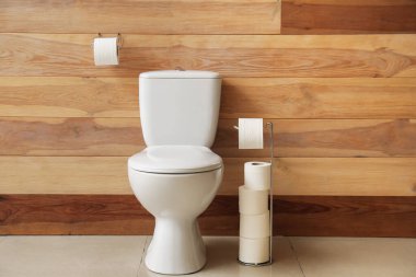 Ceramic toilet bowl and holders with paper rolls near wooden wall