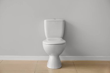 Ceramic toilet bowl near grey wall